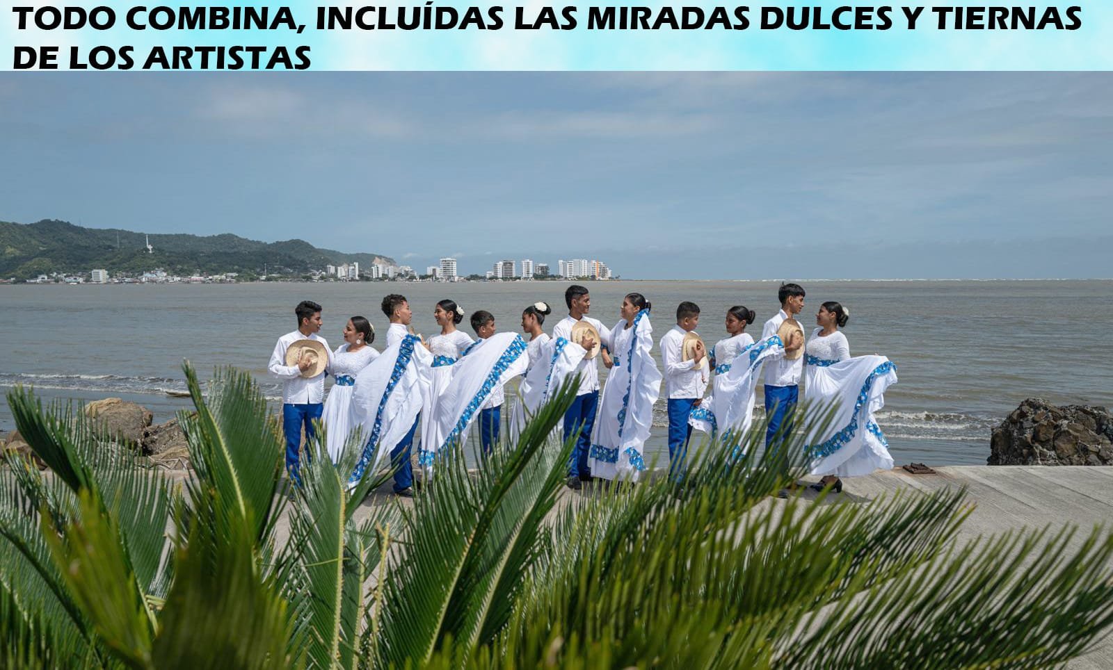 Grupo de artistas vestidos de blanco y azul posando junto al mar